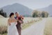 Braut und Bräutigam stehen zusammen in der Natur. Im Hintergrund sieht man eine helle alpine Landschaft.