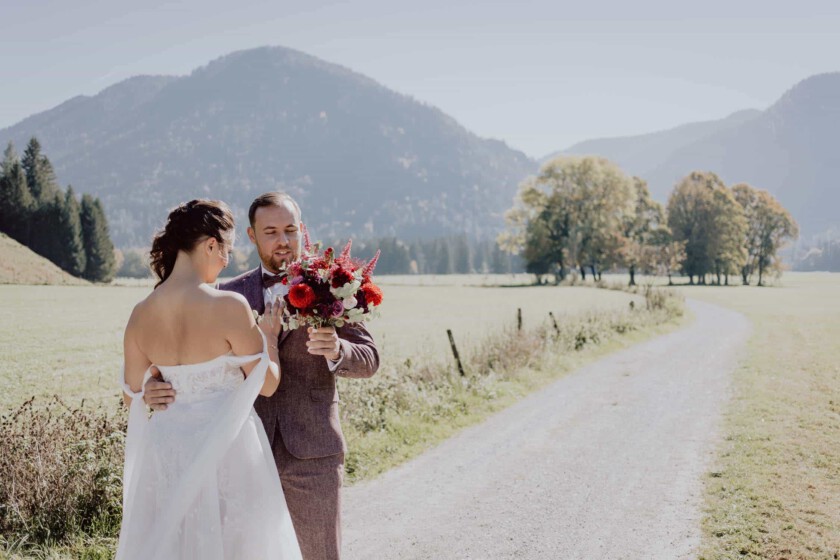 Braut und Bräutigam stehen zusammen in der Natur. Im Hintergrund sieht man eine helle alpine Landschaft.