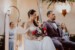 Braut und Bräutigam sitzen nebeneinander während der Trauung. Braut hält Brautstrauß in der Hand.