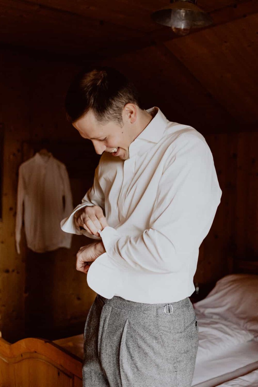 Bräutigam knöpft sich beim Getting Ready das Hemd zu in einem Zimmer der Huberspitzalm.