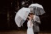 Brautpaar steht bei ihrer feier auf der Huberspitzalm vor dunklem Hintergrund, halten Regenschirme in der Hand und küssen sich