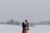 Ein Paar umarmt sich während des Paarshootings. Sie stehen in einer verschneiten Landschaft und haben Dirndl und Lederhose an.