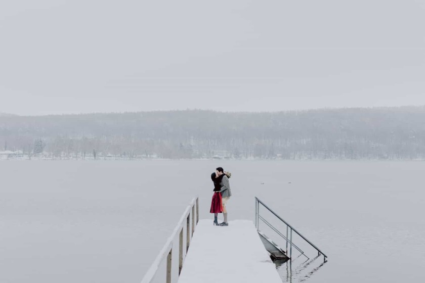 Ein paar in bayerischem Outfit umarmt sich während des Paarshootings. Sie stehen auf einem Steg vor dem Pilsensee