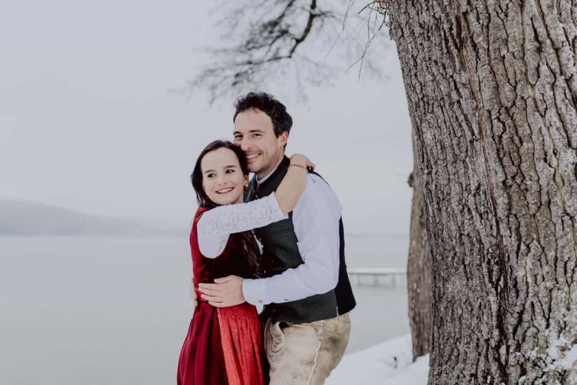 Ein paar in bayerischem Outfit umarmt sich während des Paarshootings. Sie stehe neben einem Baum.