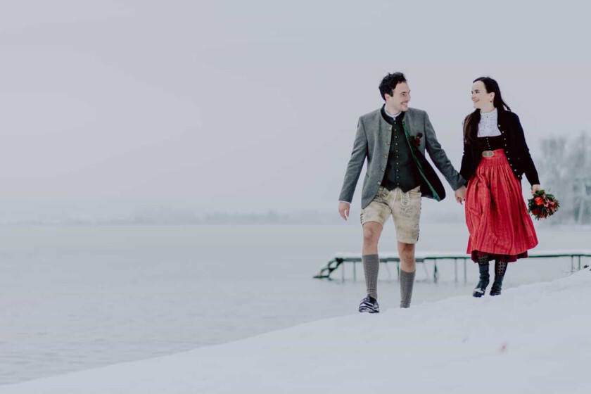 Paar geht Hand in Hand beim Paarshooting. Im Hintergrund sieht man einen See und Steg.