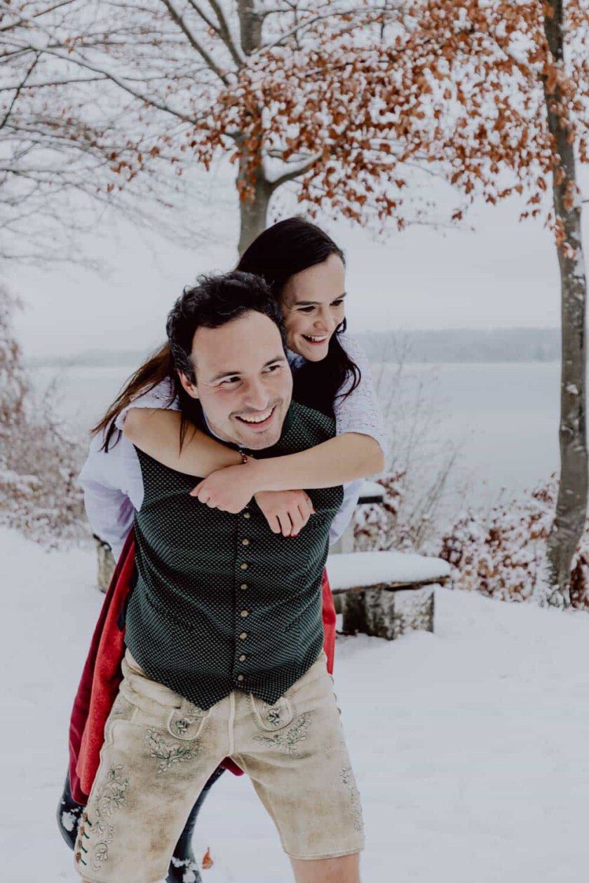 Paar nimmt sich Huckepack beim Paarshooting in winterlicher Landschaft