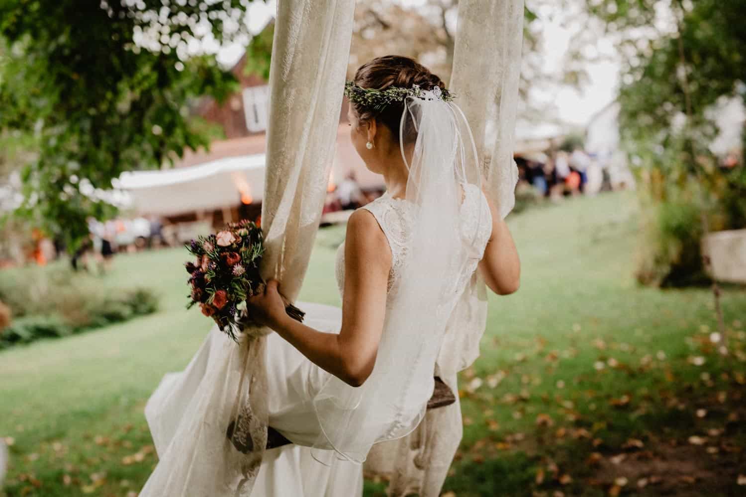 hochzeitsfotograf vintage - Aufnahme der Braut beim Schaukeln. Man sieht Brautstrauß, Haarkranz und im Hintergrund eine grüne Wiese