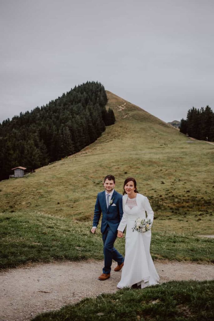 Brautpaar läuft zusammen während ihrer Hochzeit auf dem Hörnle und schauen in die Kamera.