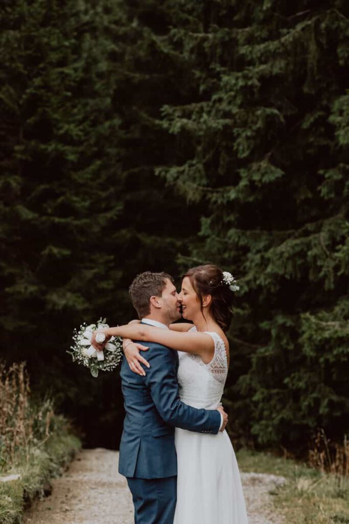 Portrait eines Brautpaares vor dunkeln Bäumen. Sie umarmen sich. Das Hochzeitsfoto ist während der Hochzeit auf dem Hörnle in Bad Kohlgrub entstanden.