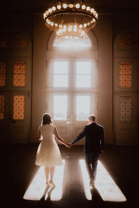 Hochzeitsfotograf Bayern Paar hält Hände im Sonnenlicht vor großen Fenstern Dokumentarische Editorial Hochzeitsfotografie