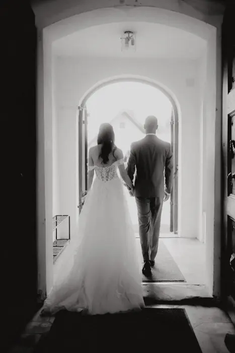 Hochzeitsfotograf Bayern Schwarzweißaufnahme eines Hochzeitspaares, das einen beleuchteten Korridor entlanggeht Dokumentarische Editorial Hochzeitsfotografie