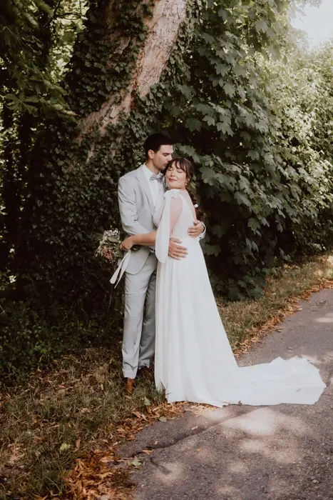 Hochzeitsfotograf Bayern Hochzeitspaar umarmt sich auf einem ländlichen Weg unter Bäumen Dokumentarische Editorial Hochzeitsfotografie